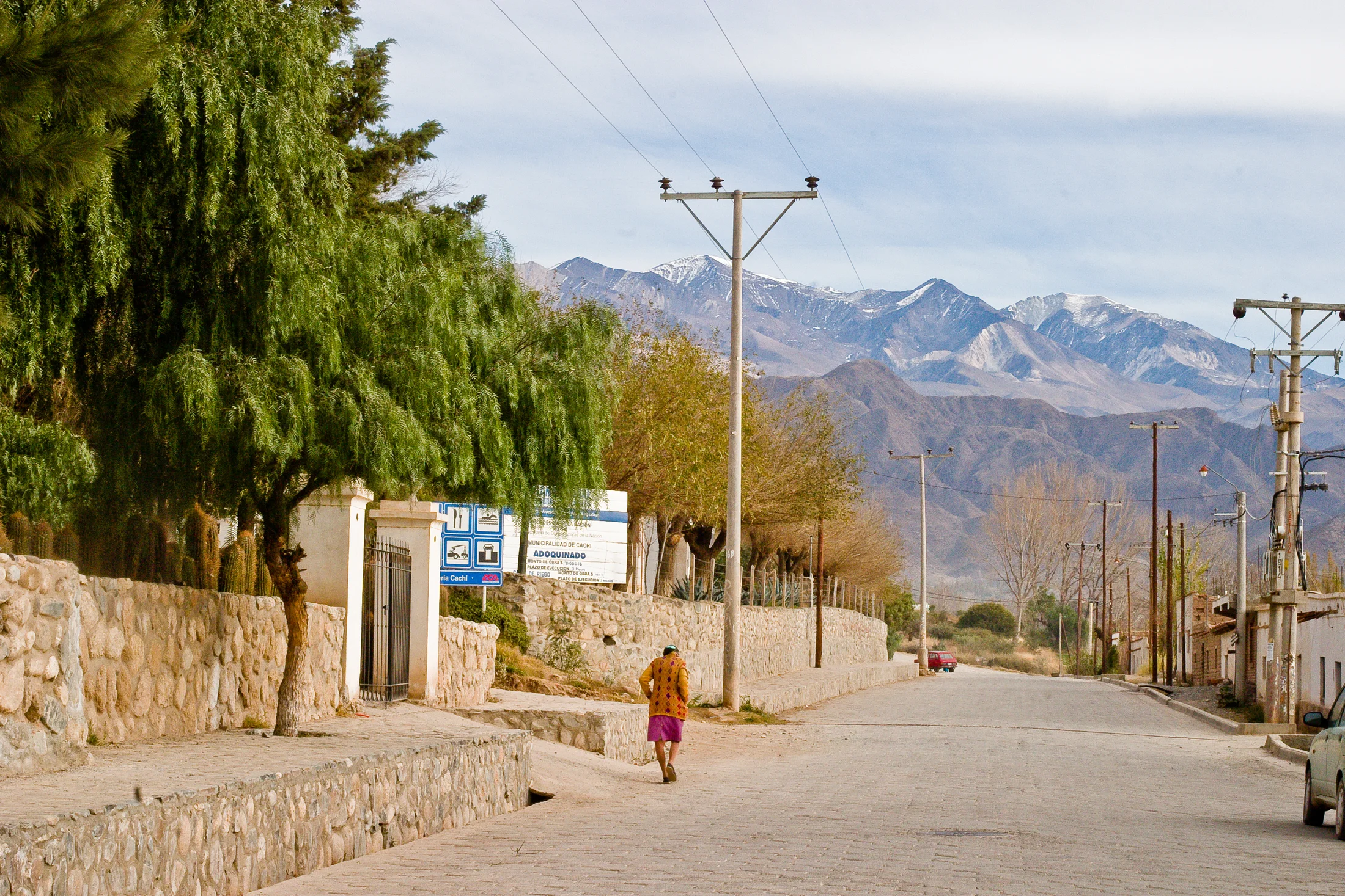 A lone figure walks down a quiet street toward mountains in Cachi