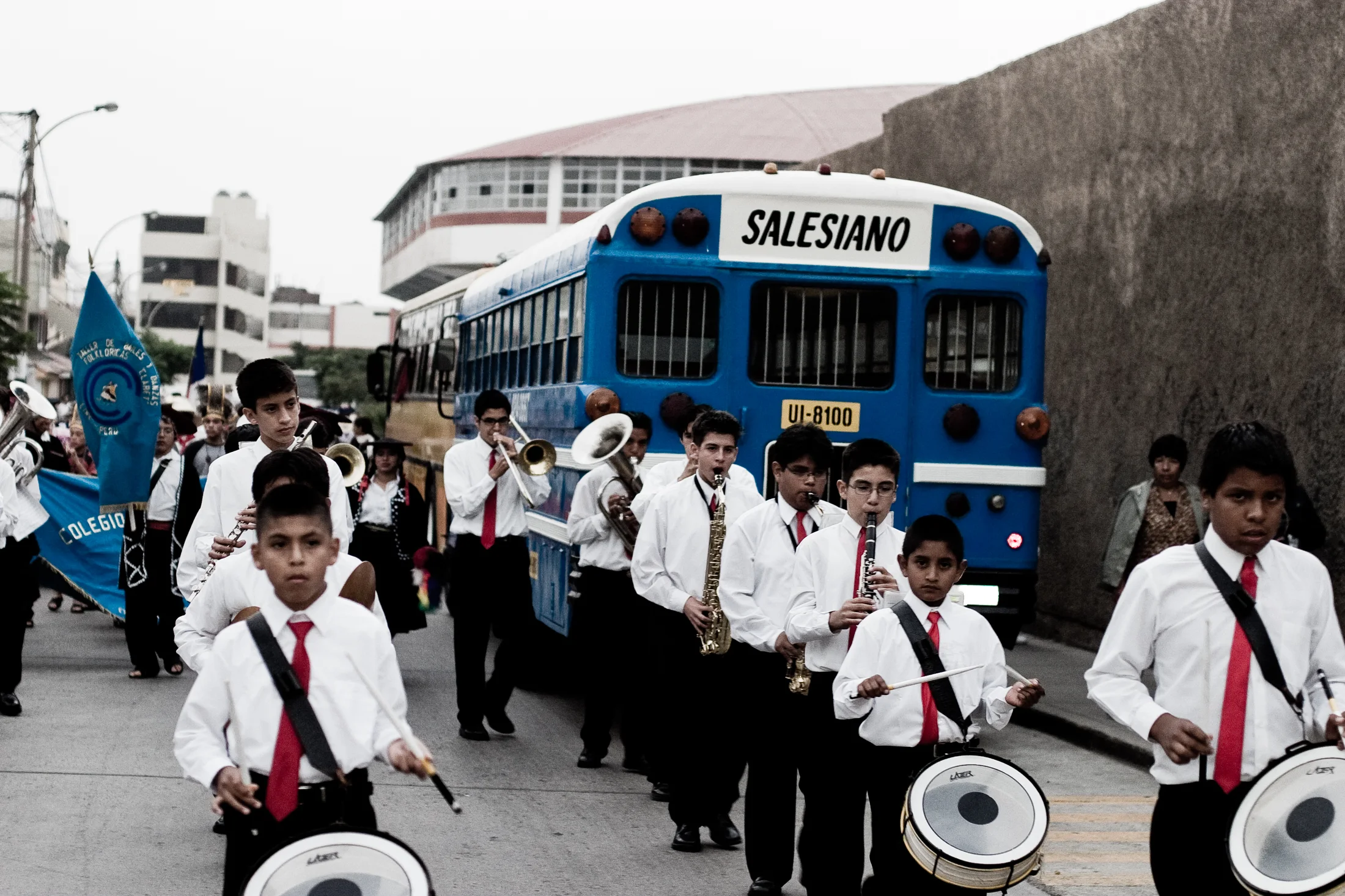 Young musicians in white shirts march beside a blue bus in Lima