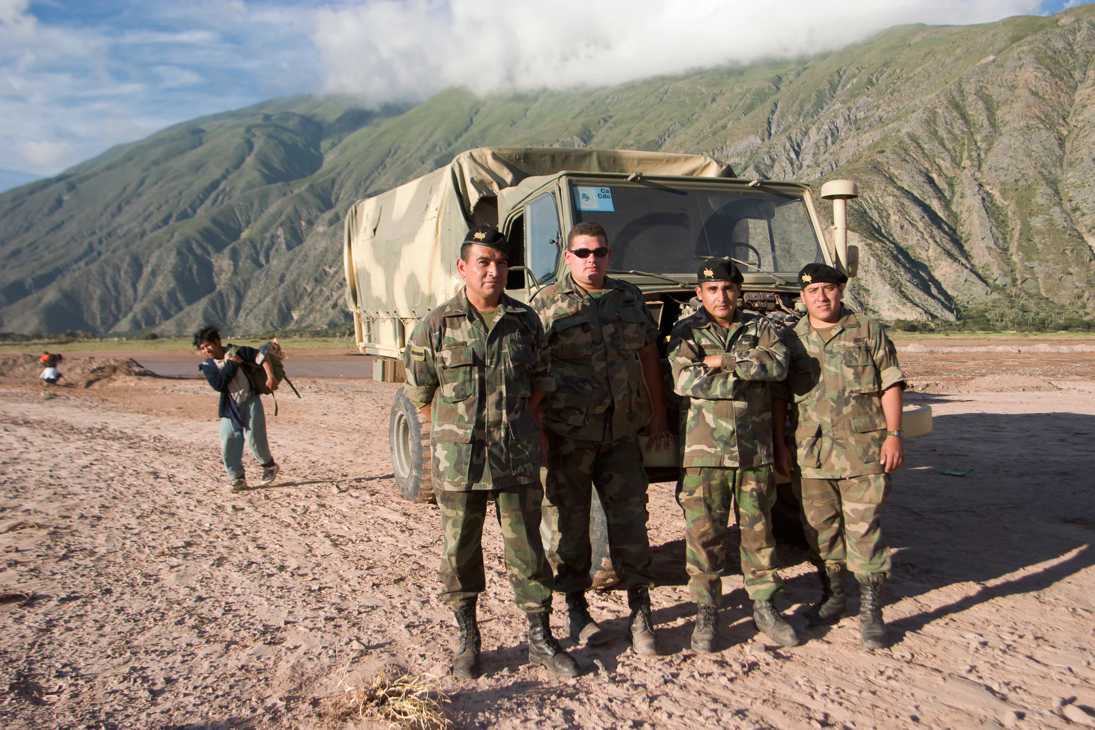 Four uniformed men stand beside a vehicle against steep mountains
