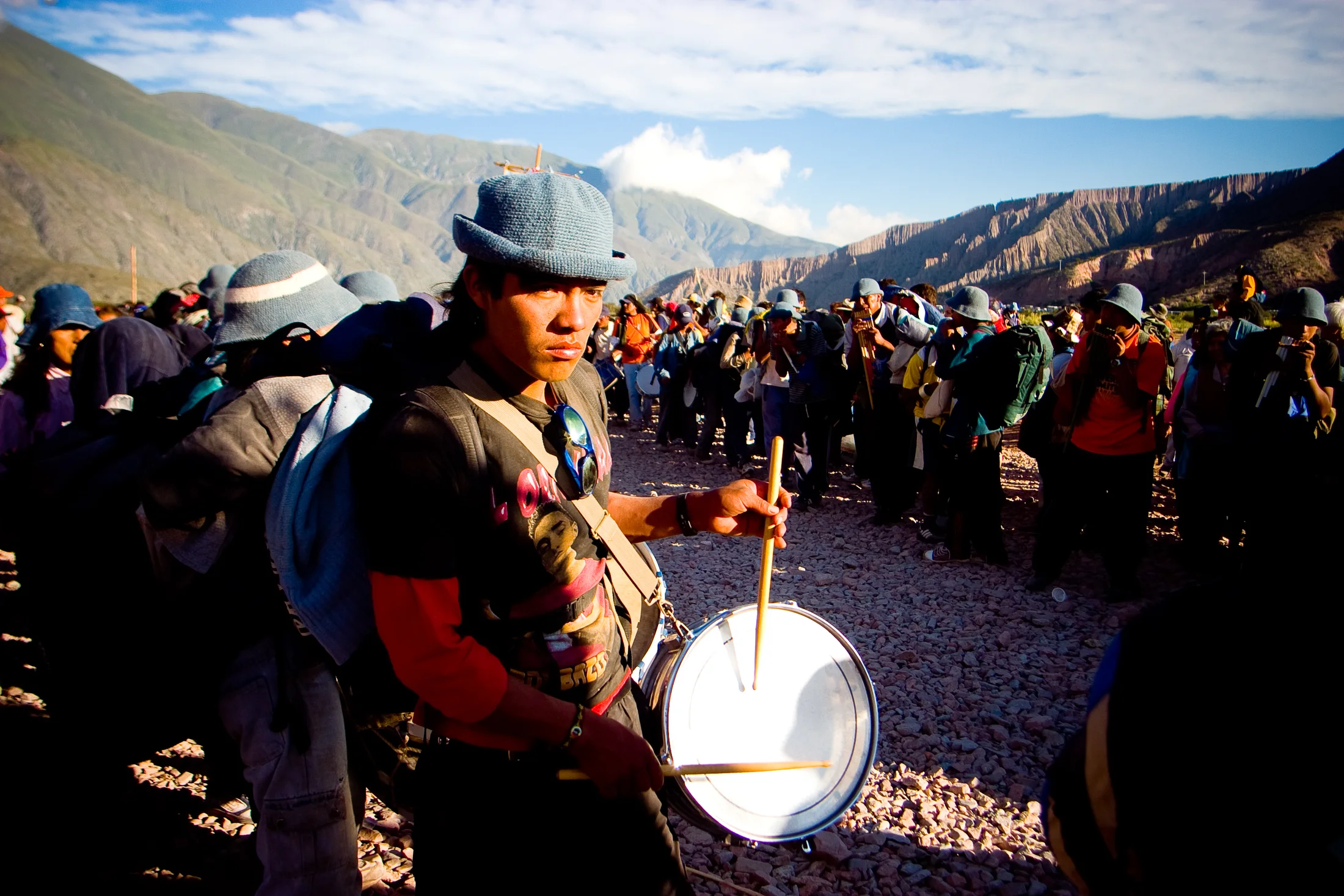 A drummer walks through a high-altitude gathering near Tumbaya