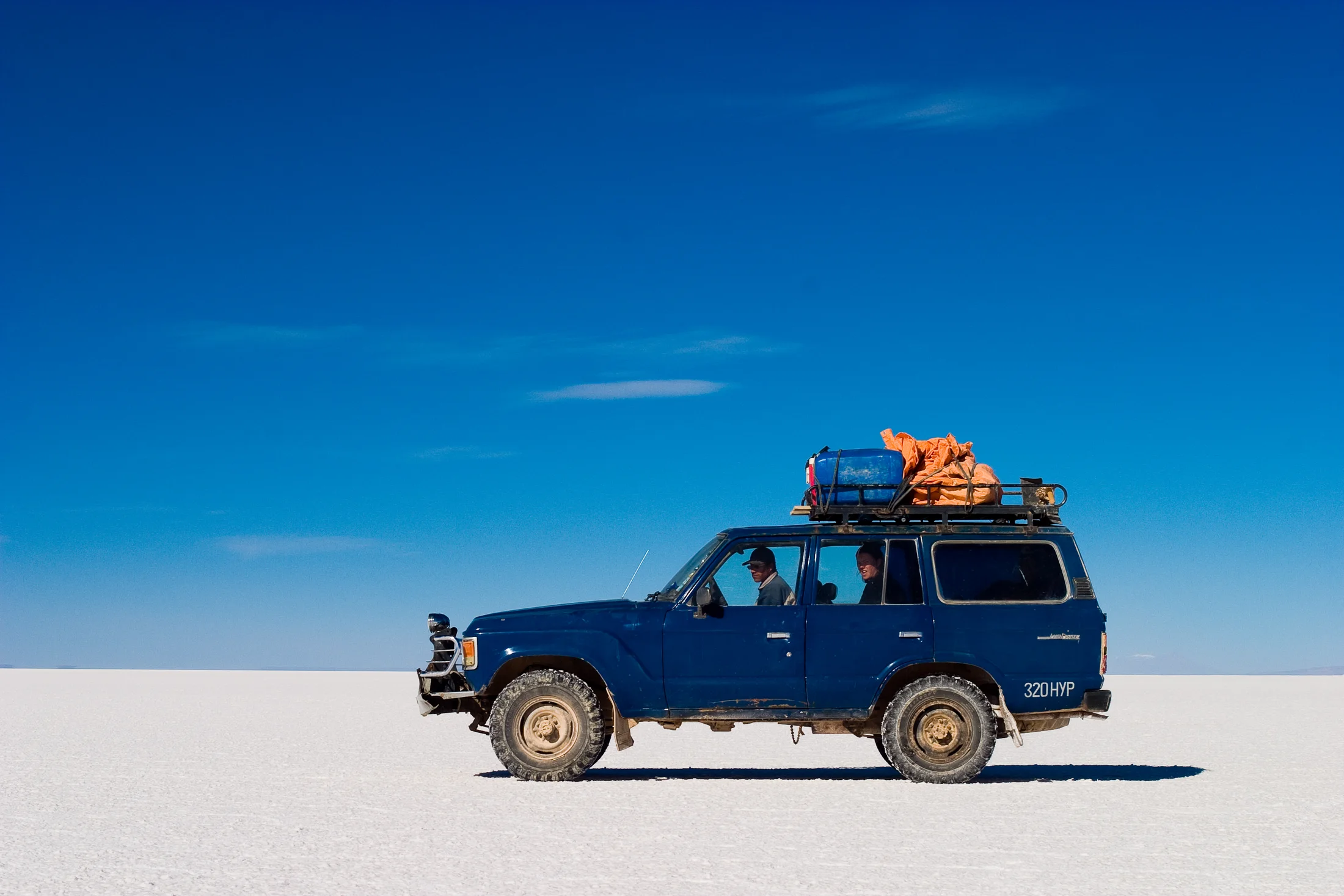 A blue four-wheel-drive vehicle crossing the Salar de Uyuni
